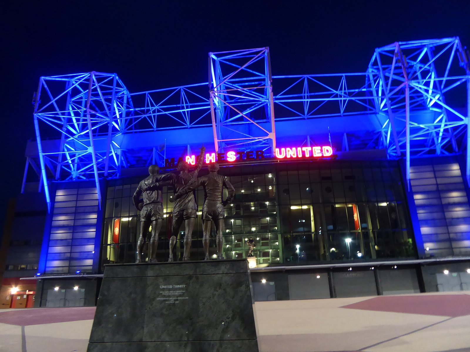 Old Trafford at night with the United Trinity statue